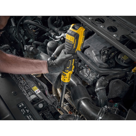 A person wearing black gloves is using a yellow and black DEWALT cordless ratchet tool to work on a car engine.