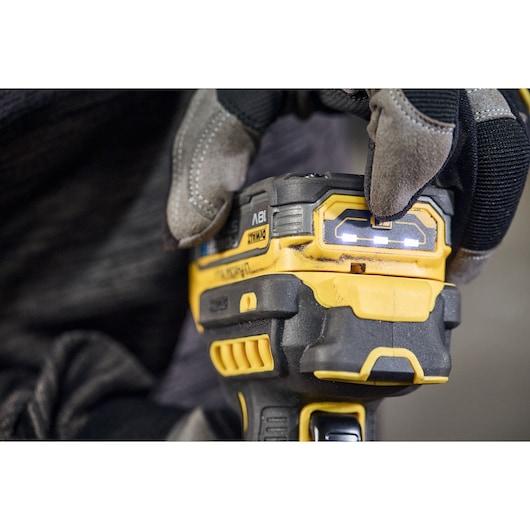 Close-up of a gloved hand holding a DEWALT cordless power tool with LED indicator lights illuminated on the battery pack.