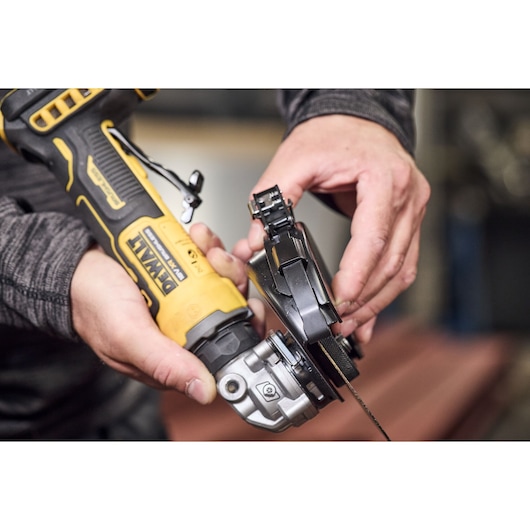 A person is adjusting a DEWALT cordless angle grinder, model DCG404S2T, with a grinding disc attached.