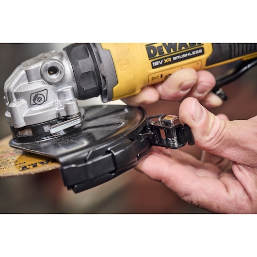 Close-up view of hands adjusting the protective guard on a DEWALT 18V XR Brushless angle grinder.