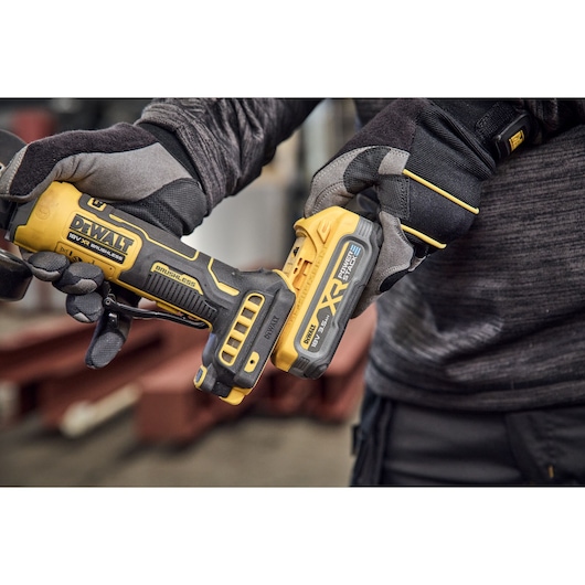 Close-up of a person wearing work gloves holding a DEWALT 18V XR brushless power tool, with focus on the tool and battery pack.