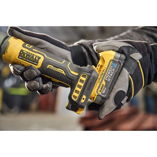 Close-up of a person wearing work gloves holding a DEWALT 18V XR Brushless Power Tool with a DEWALT PowerStack battery attached.