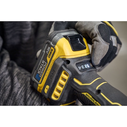 Close-up image of a DEWALT DCG420N cordless power tool held by a person wearing work gloves. The tool features an 18V POWERSTACK battery and brushless motor.