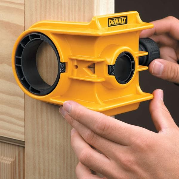 Una persona sta utilizzando un kit di installazione per serrature di porte DEWALT giallo per allineare e segnare un foro su una cornice di porta in legno.