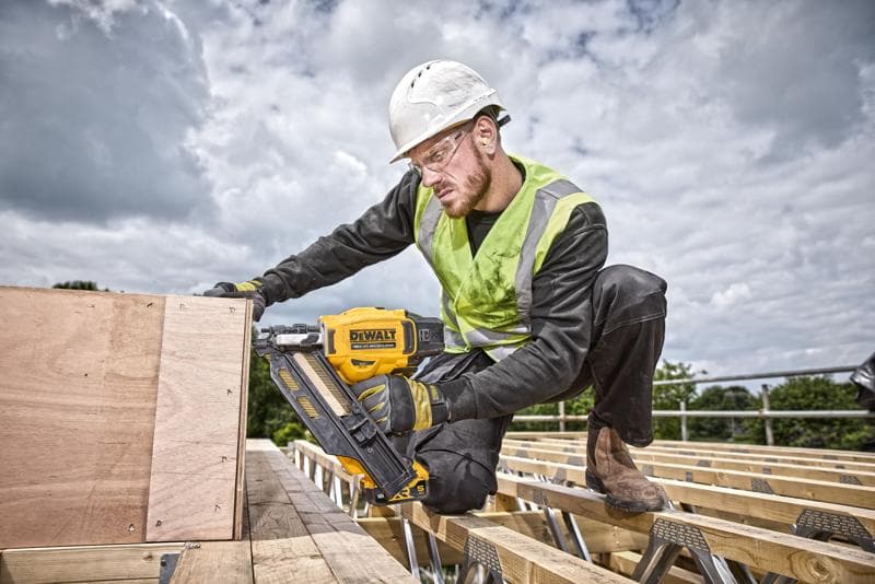Persona usa una chiodatrice DEWALT DCN930N su tavole di legno in cantiere, indossa equipaggiamento di sicurezza.