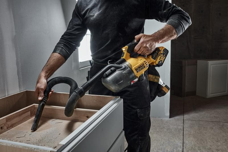 Persona pulisce una credenza in legno con un aspirapolvere portatile DEWALT senza fili durante lavori.