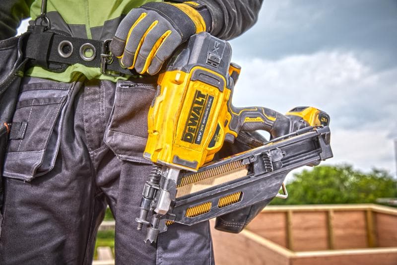 Persona con chiodatrice DEWALT DCN930N, indossa guanti e abbigliamento da lavoro in un cantiere all'aperto.
