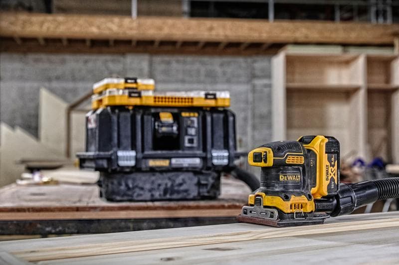 Levigatrice DEWALT senza fili su legno, scatola di stoccaggio sullo sfondo in un'officina.