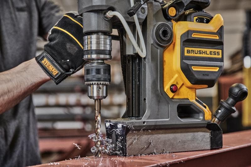 Persona usa trapano magnetico DEWALT brushless per forare metallo, producendo trucioli sul tavolo.