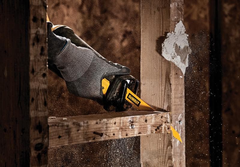 Primo piano di una mano con guanto grigio che utilizza un seghetto alternativo DEWALT per tagliare una trave di legno, con segatura che si disperde nell'aria.