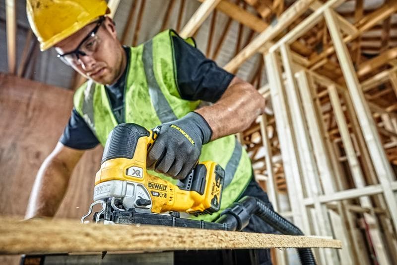 Seghetto DEWALT DCS334P2 taglia legno in cantiere, operatore con abbigliamento di sicurezza.