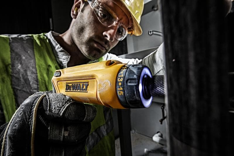 Persona usa cacciavite DEWALT DCF680G2 giallo con guanto in ambiente industriale.