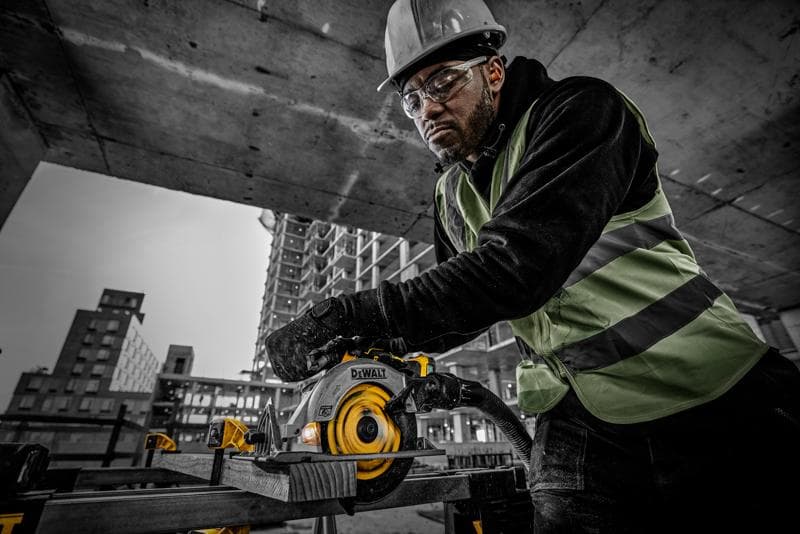 Persona usa sega circolare DEWALT DCS565NT in cantiere, con abbigliamento protettivo e taglia legno.