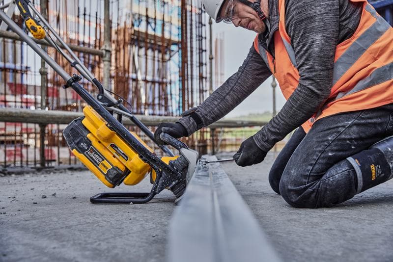 Operaio usa un utensile DEWALT giallo per tagliare metallo in cantiere, indossa giubbotto arancione e protezioni.