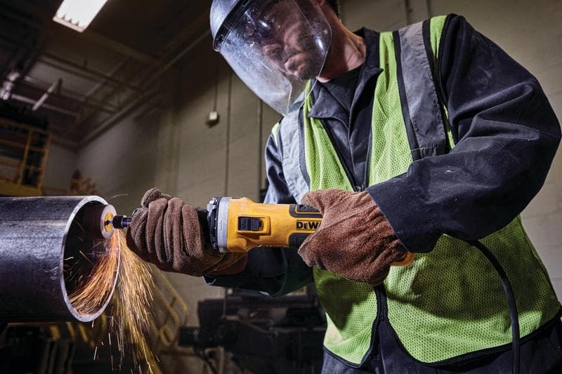 Operaio usa una smerigliatrice DEWALT su tubo metallico, scintille, con guanti e dispositivi di sicurezza.