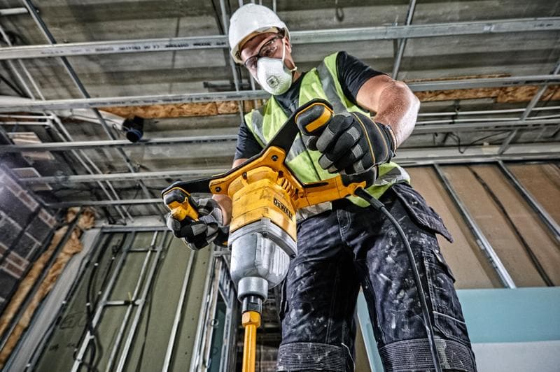 Persona usa miscelatore DEWALT DWD241 in cantiere, indossando dispositivi di sicurezza e guanti.