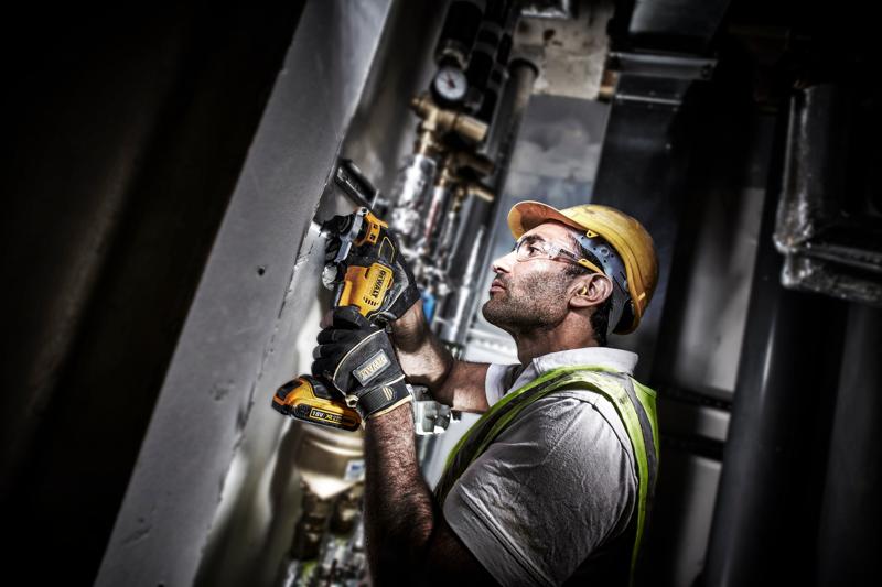 Operaio usa un DEWALT DCS355D2 su una parete, indossando equipaggiamento di sicurezza e guanti.