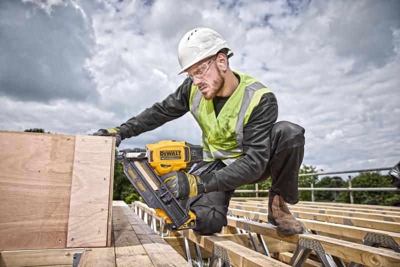 Persona usa una chiodatrice DEWALT DCN930N su tavole di legno in cantiere, indossa equipaggiamento di sicurezza.
