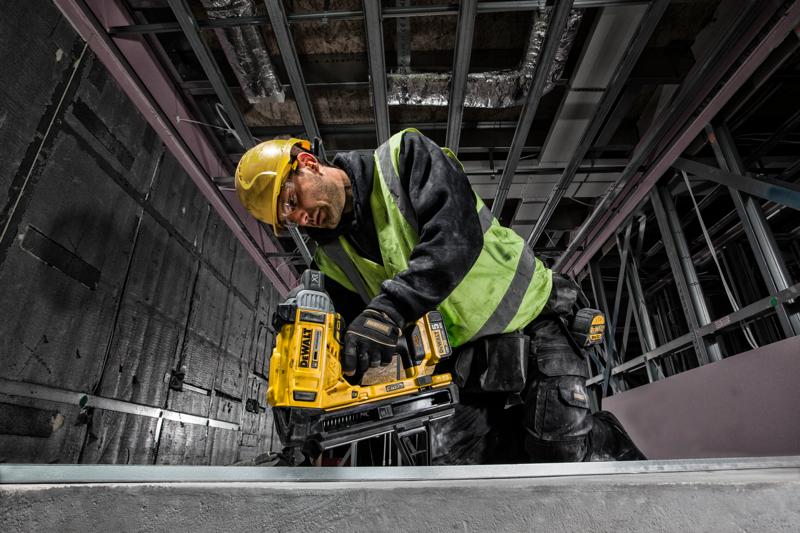 Operaio usa DEWALT DCN890P2 chiodatrice, con casco e gilet in un cantiere.