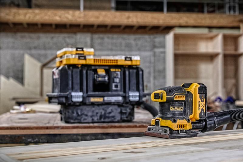 Levigatrice DEWALT senza fili su legno, scatola di stoccaggio sullo sfondo in un'officina.