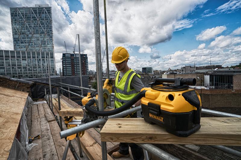 Aspirapolvere DEWALT DCV584 su cantiere sul tetto con operaio e edifici urbani sullo sfondo.