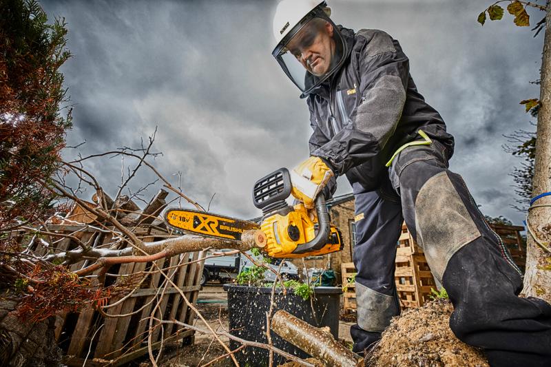 Persona con protezione usa motosega DEWALT per tagliare rami all'aperto in una giornata nuvolosa.