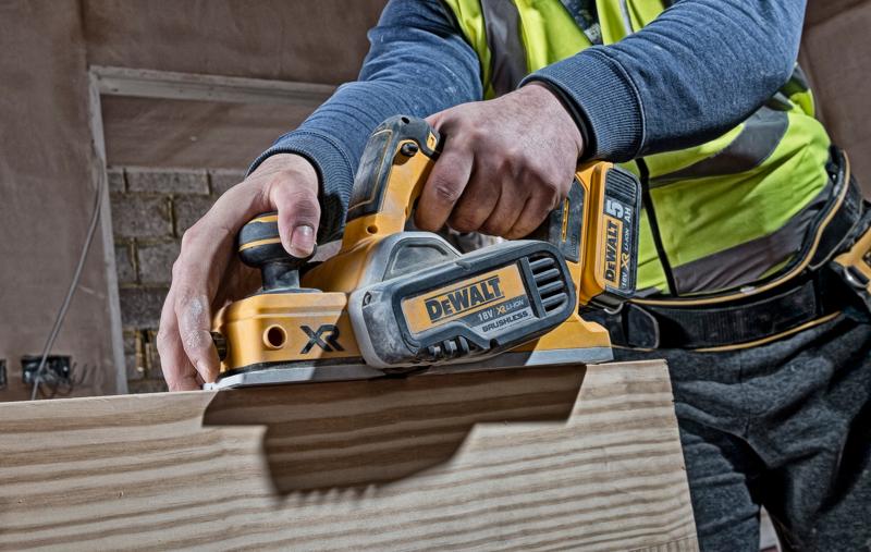 Persona usa una pialla a batteria DEWALT DCP580N su legno in un cantiere.