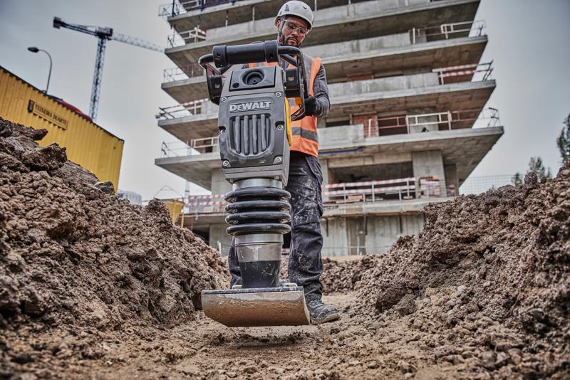 Compattatore DEWALT su cantiere, usato da operatore con equipaggiamento di sicurezza, tra terra e edifici.