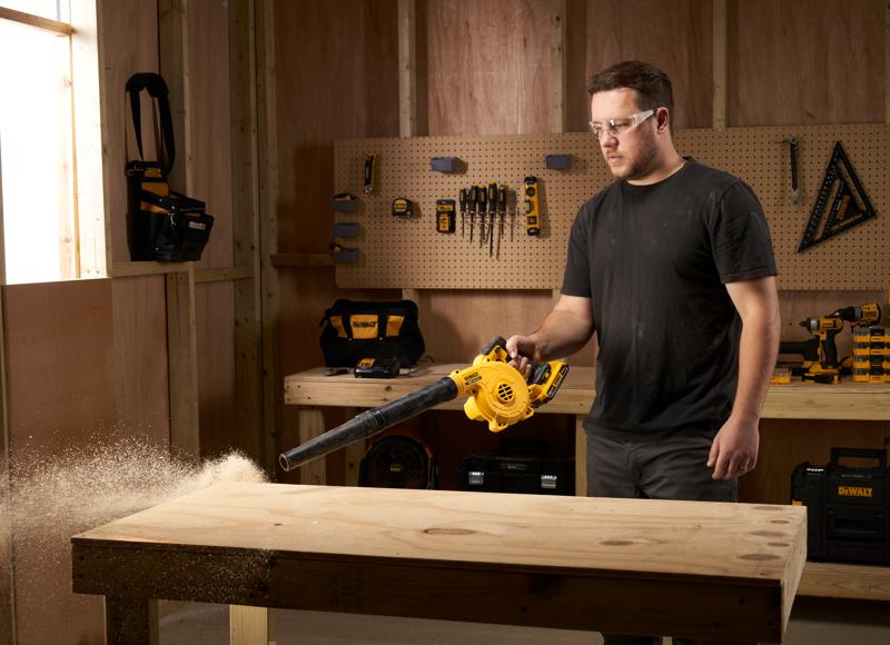 Persona usa un soffiatore DEWALT DCV100 per pulire la segatura da un banco da lavoro in una officina.