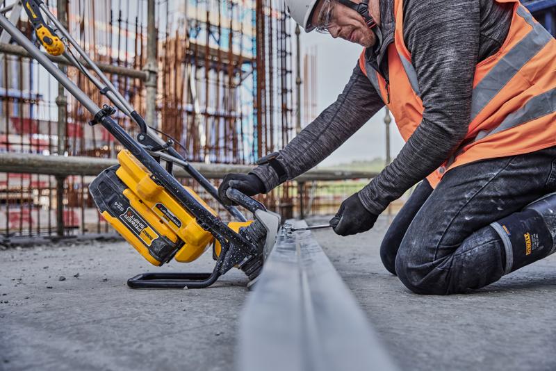 Operaio usa un utensile DEWALT giallo per tagliare metallo in cantiere, indossa giubbotto arancione e protezioni.