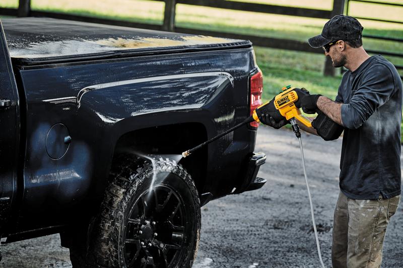 Una persona utilizza una idropulitrice cordless DEWALT DCPW550B per pulire la ruota e il lato di un pickup nero all’aperto.