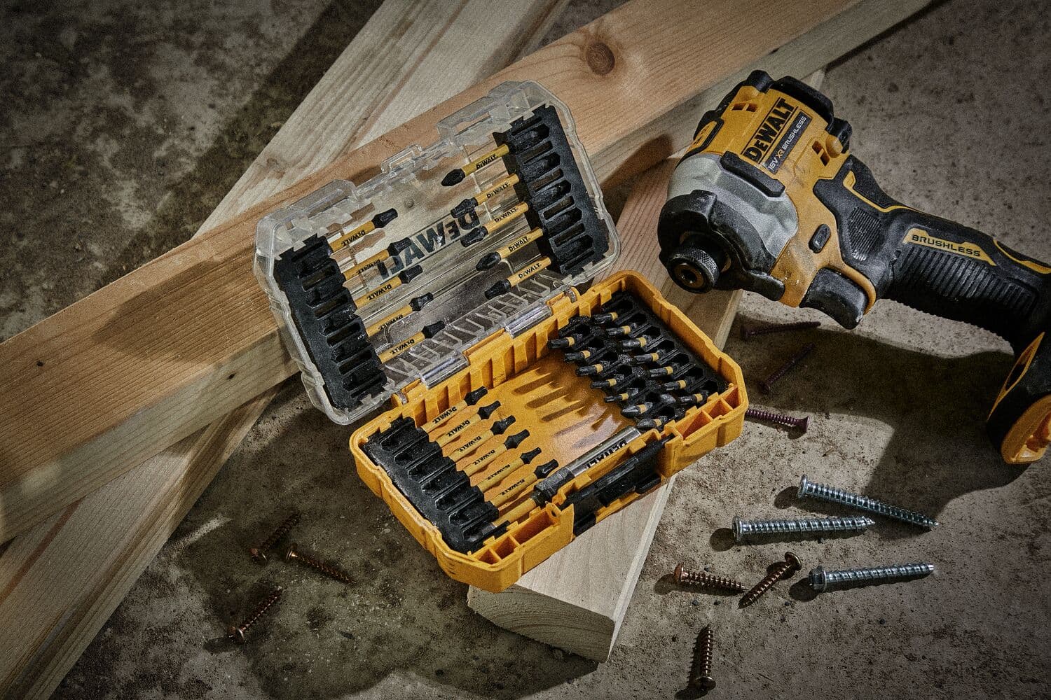 Trapano DEWALT e set di punte con viti su pavimento da officina vicino assi di legno.